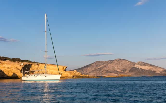 Cockpit of a sailing yacht cruising past green Ionian cliffs